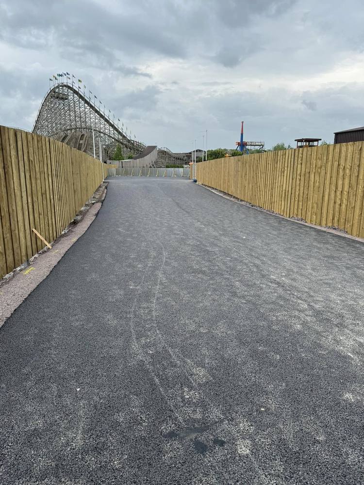 A wide finished asphalt access road running between new timber fencing.