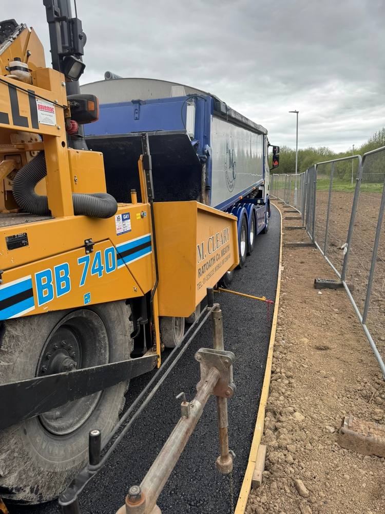 A tipper reversing onto the paver hopper to feed material directly into the machine.